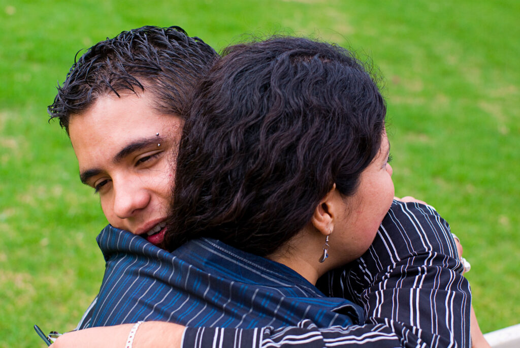 A teen of color embraces their parent.